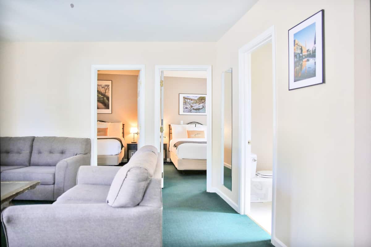 A hotel room with a grey sofa, a bed, a nightstand, and a framed picture on the wall.