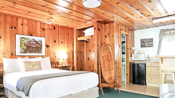A wooden cabin-style room with a bed, a desk, a mirror, and a small kitchen area. - Sierra Mountain Inn (Grass Valley)