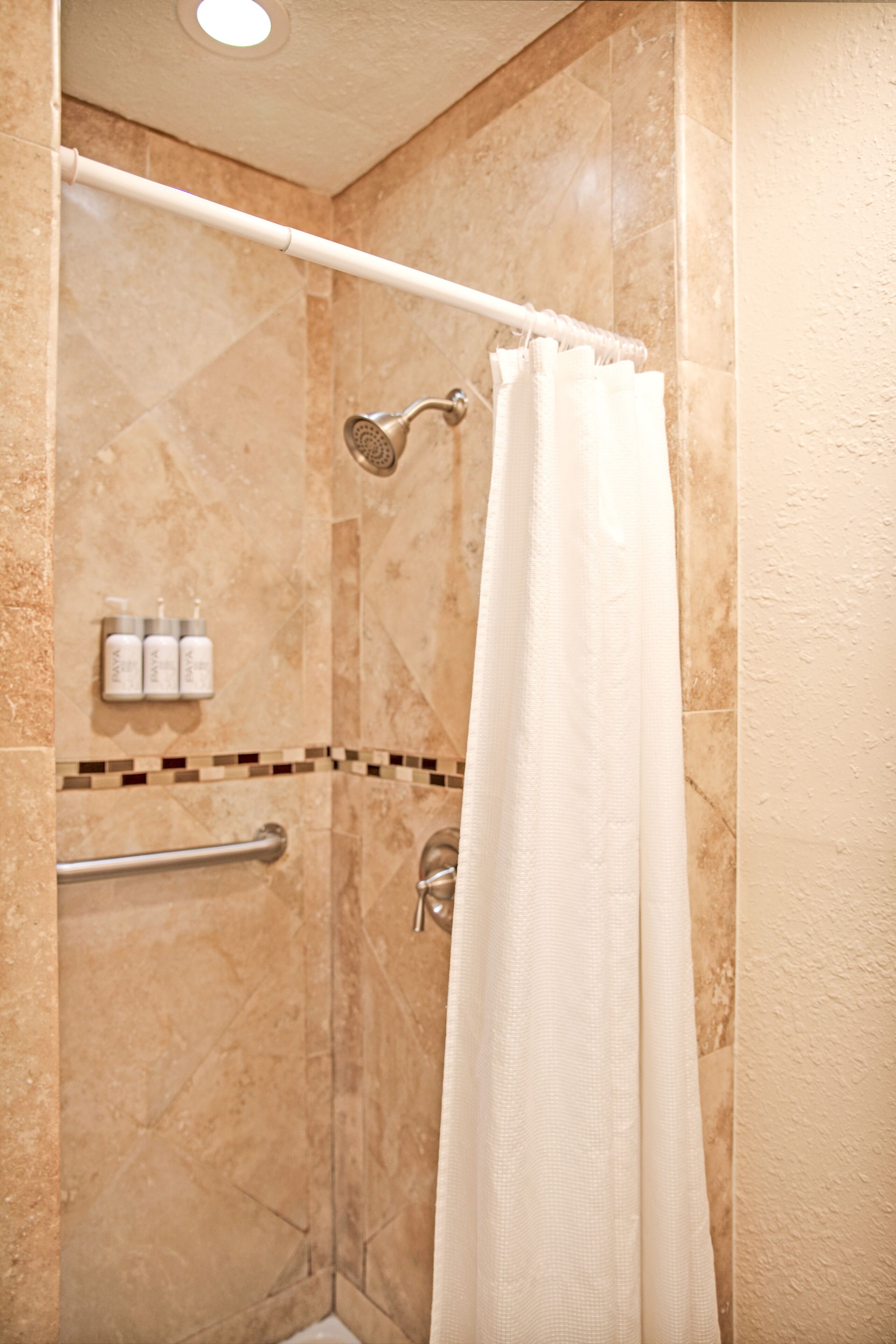 A shower area with a beige tiled wall, a white shower curtain, and a handheld showerhead.