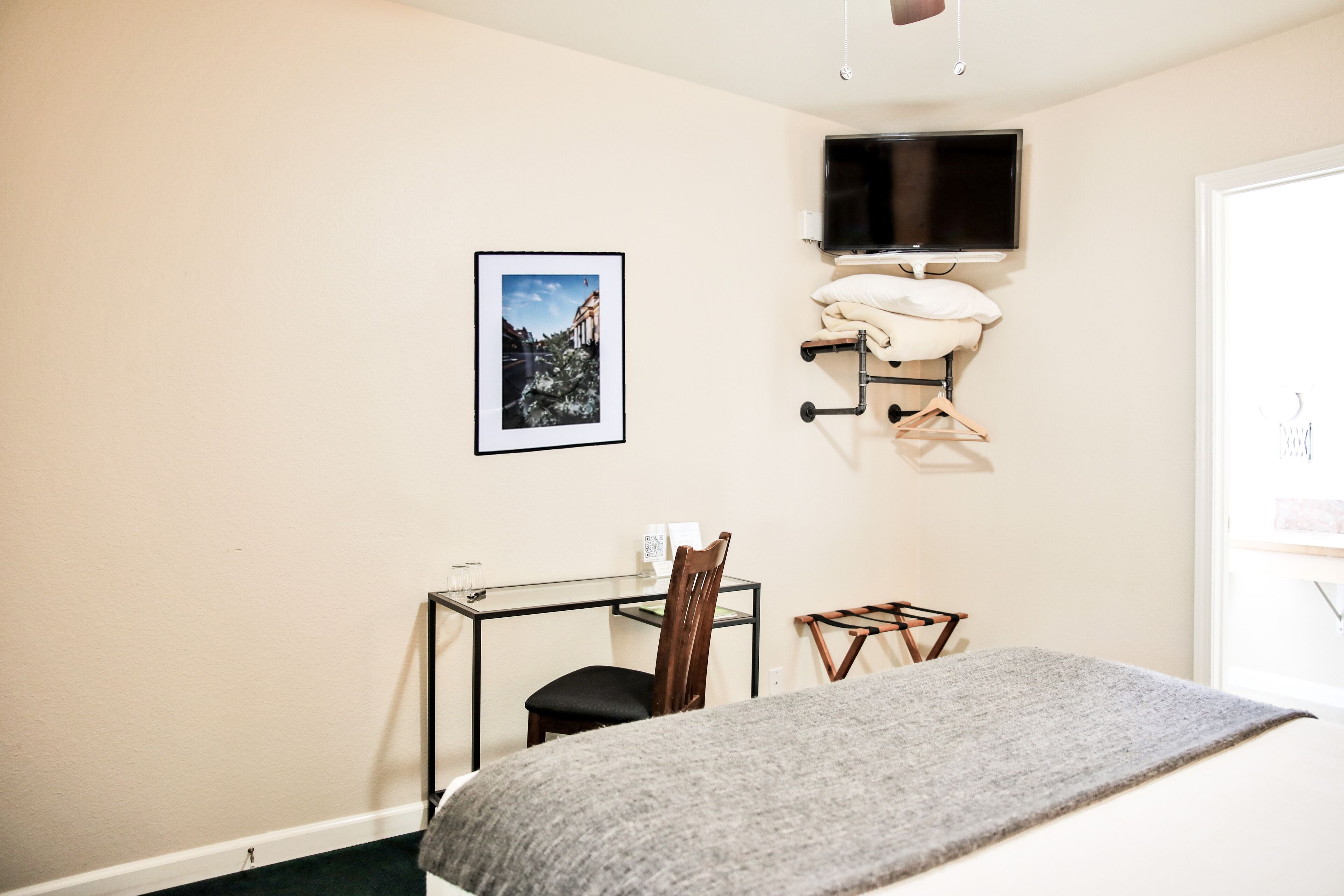 Een slaapkamer met een bed, een bureau met stoel, een aan de muur bevestigde televisie en een ingelijst schilderij.