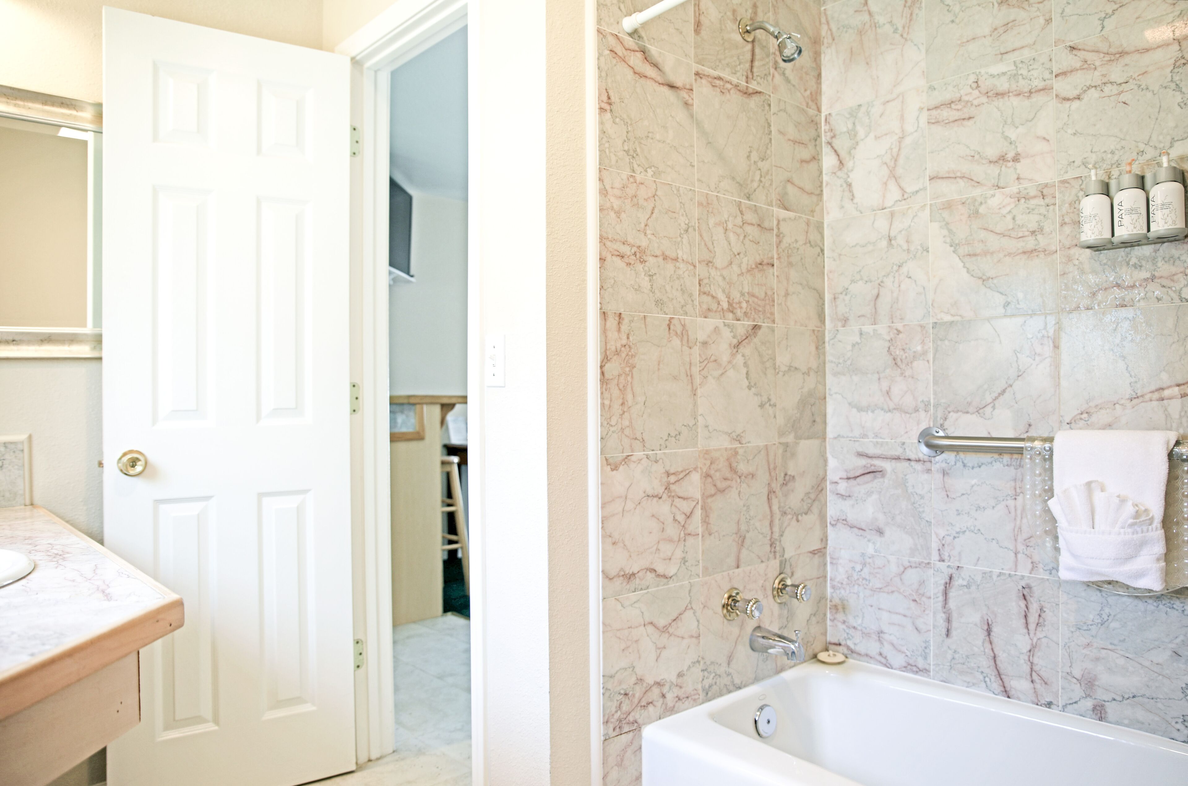 A bathroom with a marble shower wall, a bathtub, and a vanity with a sink.