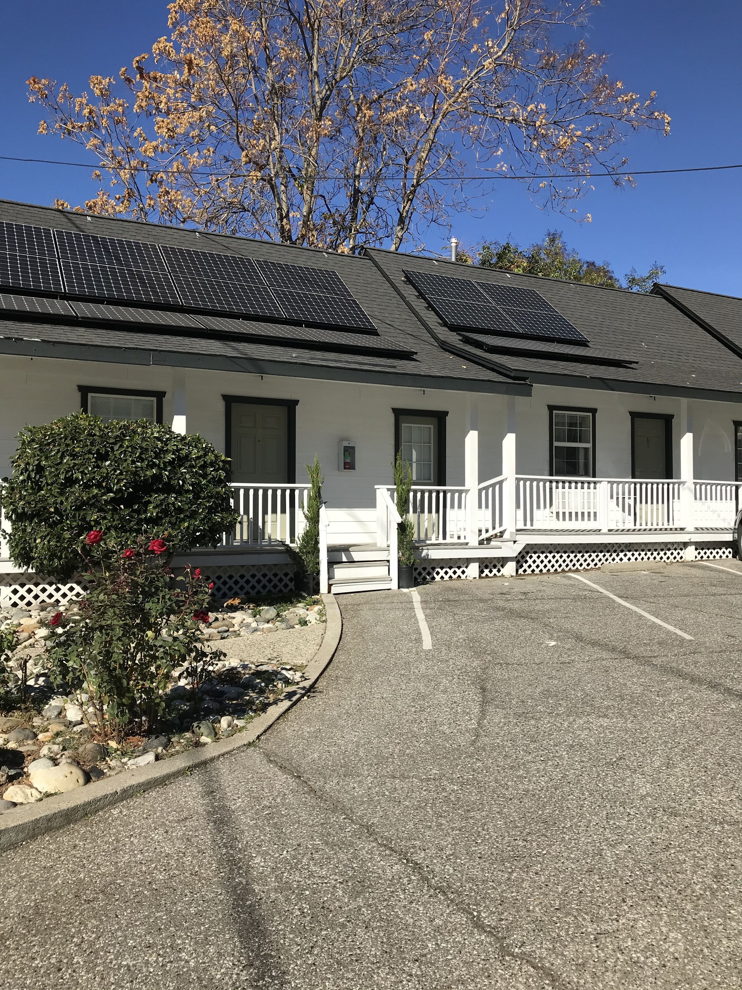 Un edificio con paneles solares en el techo, fachada blanca y un estacionamiento con un pequeño jardín.
