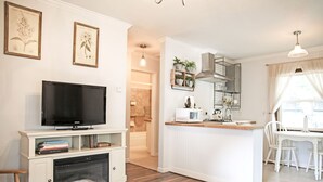 A modern living room with a flat-screen TV, a fireplace, and a dining area with a kitchen in the background. - Sierra Mountain Inn (Grass Valley)