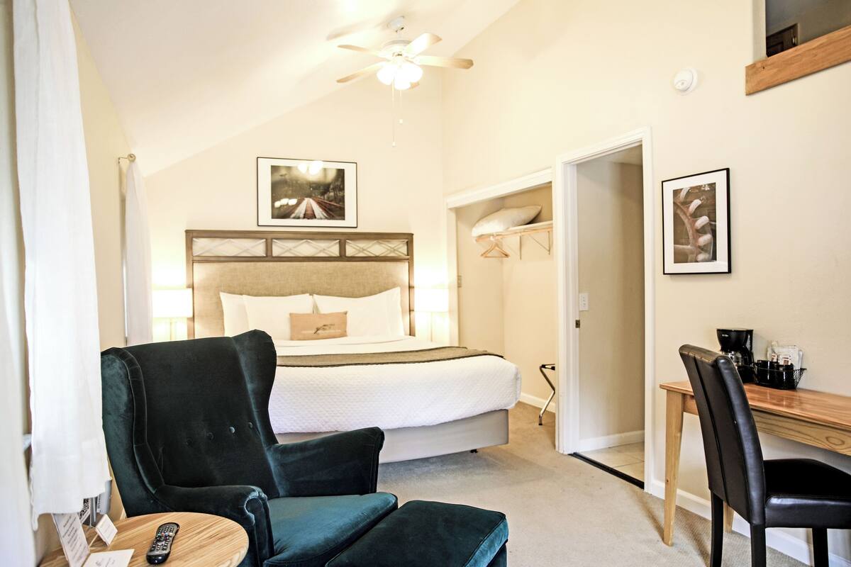 A hotel room with a bed, a desk, a chair, and a ceiling fan.