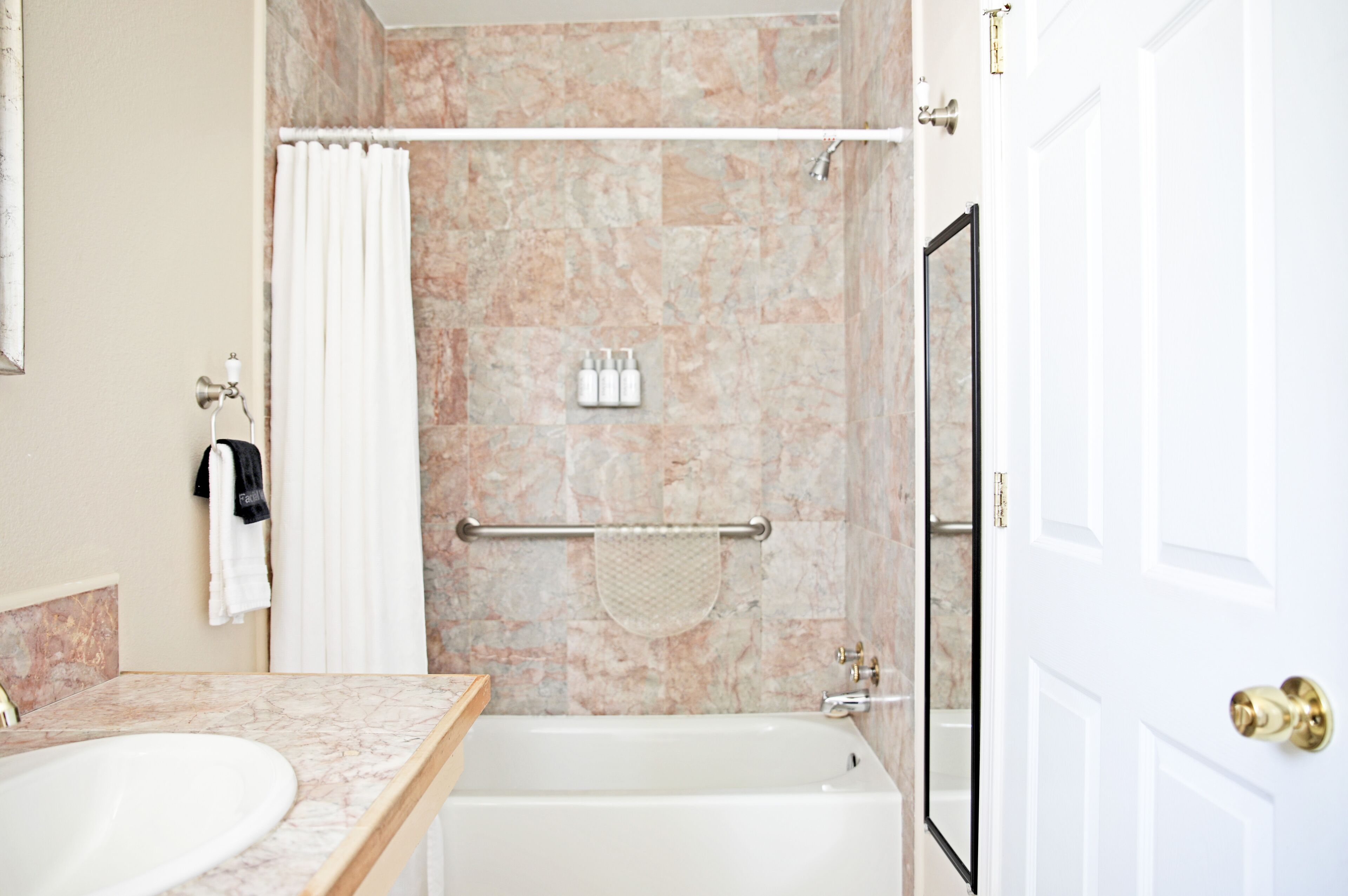 A bathroom with a marble sink, a bathtub, a shower with a glass door, and toiletries on the wall.