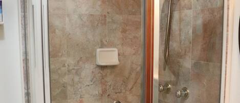 A glass-enclosed shower stall with a handheld showerhead, a glass door, and a handrail.