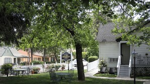 A hotel with a white exterior, a signboard, a lawn with a table and chairs, and a white picket fence. - Sierra Mountain Inn (Grass Valley)