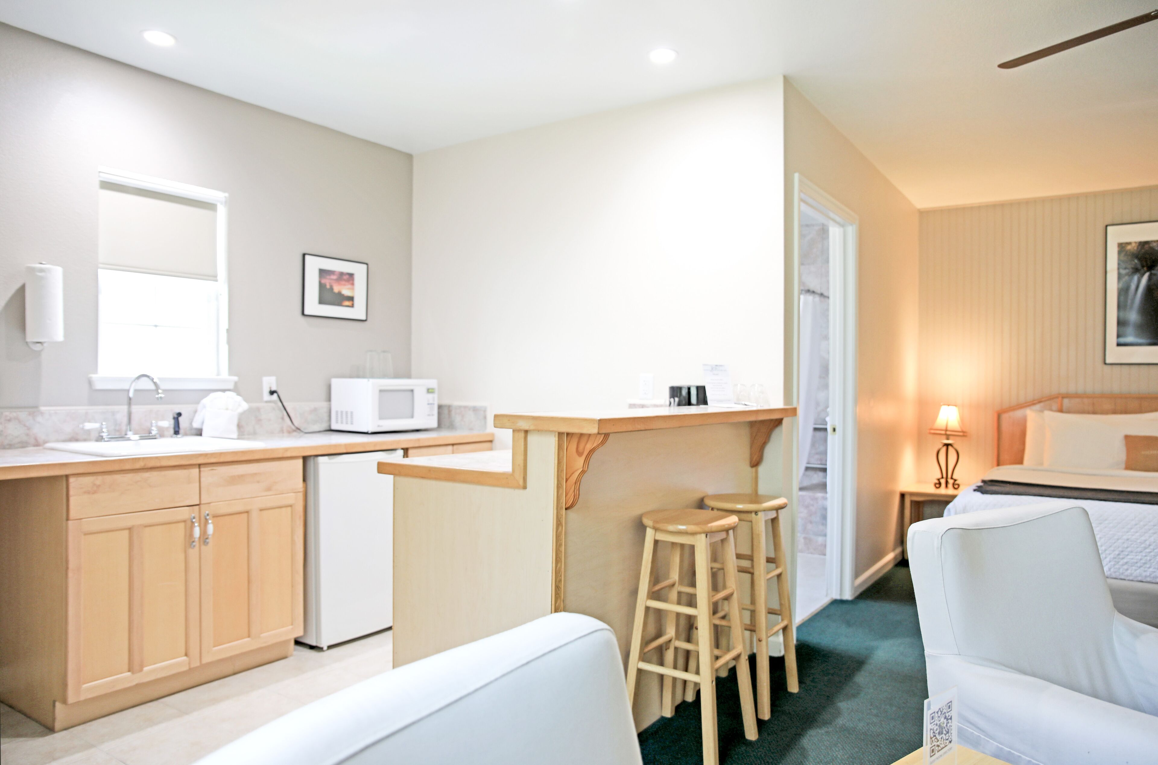 A compact hotel room with a kitchenette, a bed, a small sitting area, and a bathroom.