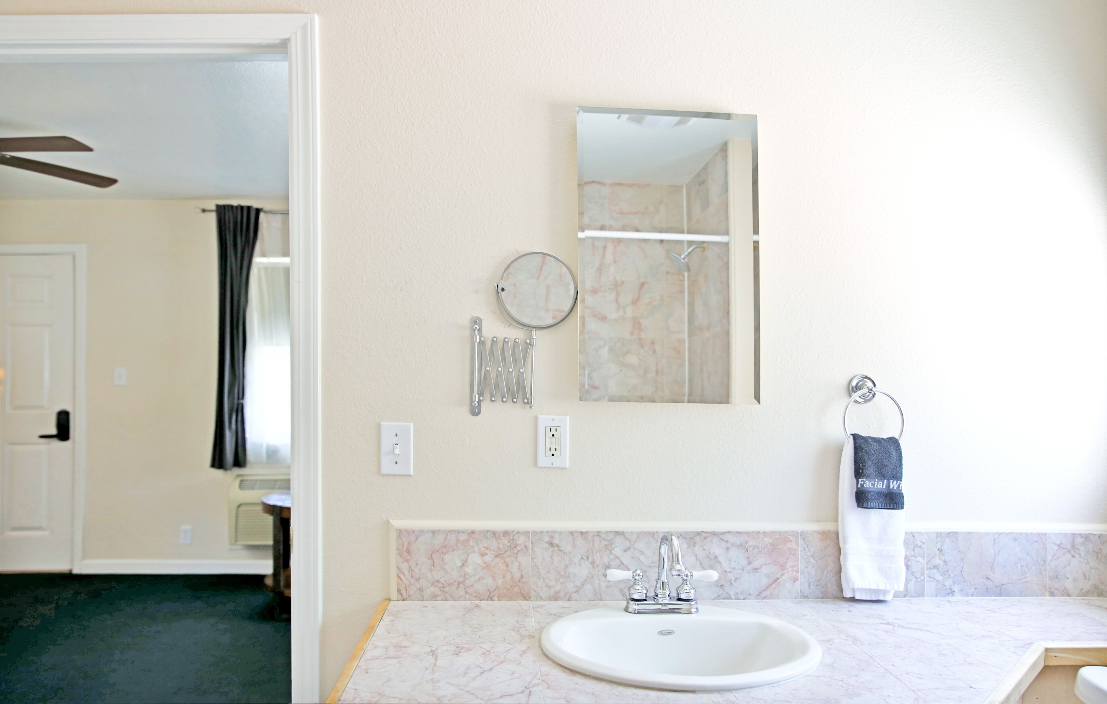 A bathroom with a marble sink, a mirror, a towel rack, and a shower visible in the background.