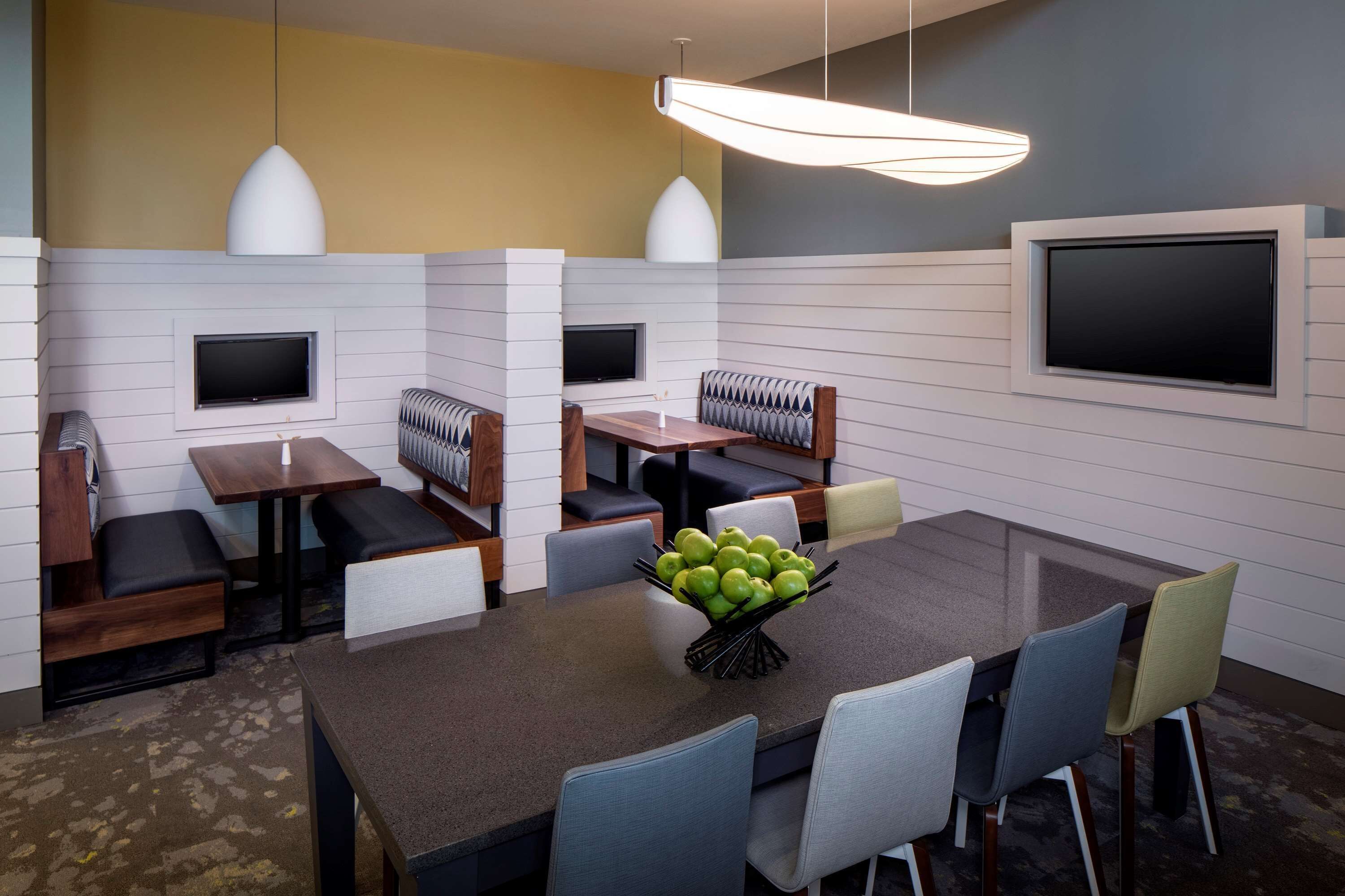 A modern dining area with a central table, seating, and a fruit bowl.