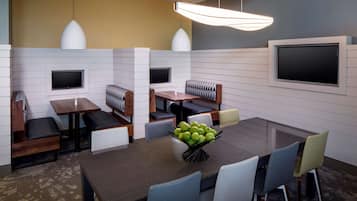 A modern dining area with a central table, seating, and a fruit bowl.