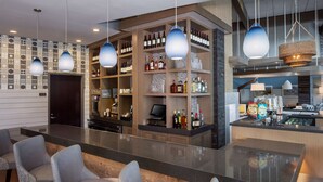 A modern bar area with a long counter, multiple seating options, and a variety of bottles and glasses on shelves. - Hyatt Place Long Island East End (Riverhead)