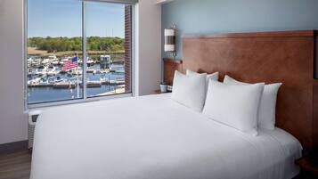 A hotel room with a large bed, a wooden headboard, and a view of a marina with boats and an American flag.