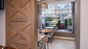 A dining area with wooden paneling, a patterned floor, and a view of outdoor seating through large windows. - Hyatt Place Long Island East End (Riverhead)