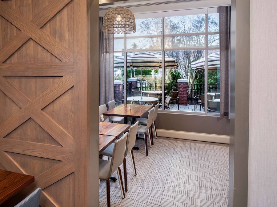 A dining area with wooden paneling, a patterned floor, and a view of outdoor seating through large windows.