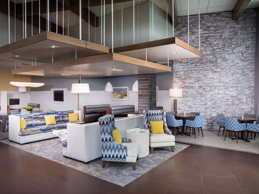 A modern lounge area with sofas, armchairs, and tables, featuring a brick wall and hanging pendant lights.
