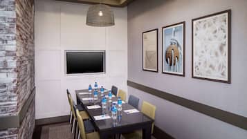 A conference room with a long table, chairs, water bottles, a flat-screen TV, and framed artwork on the walls.