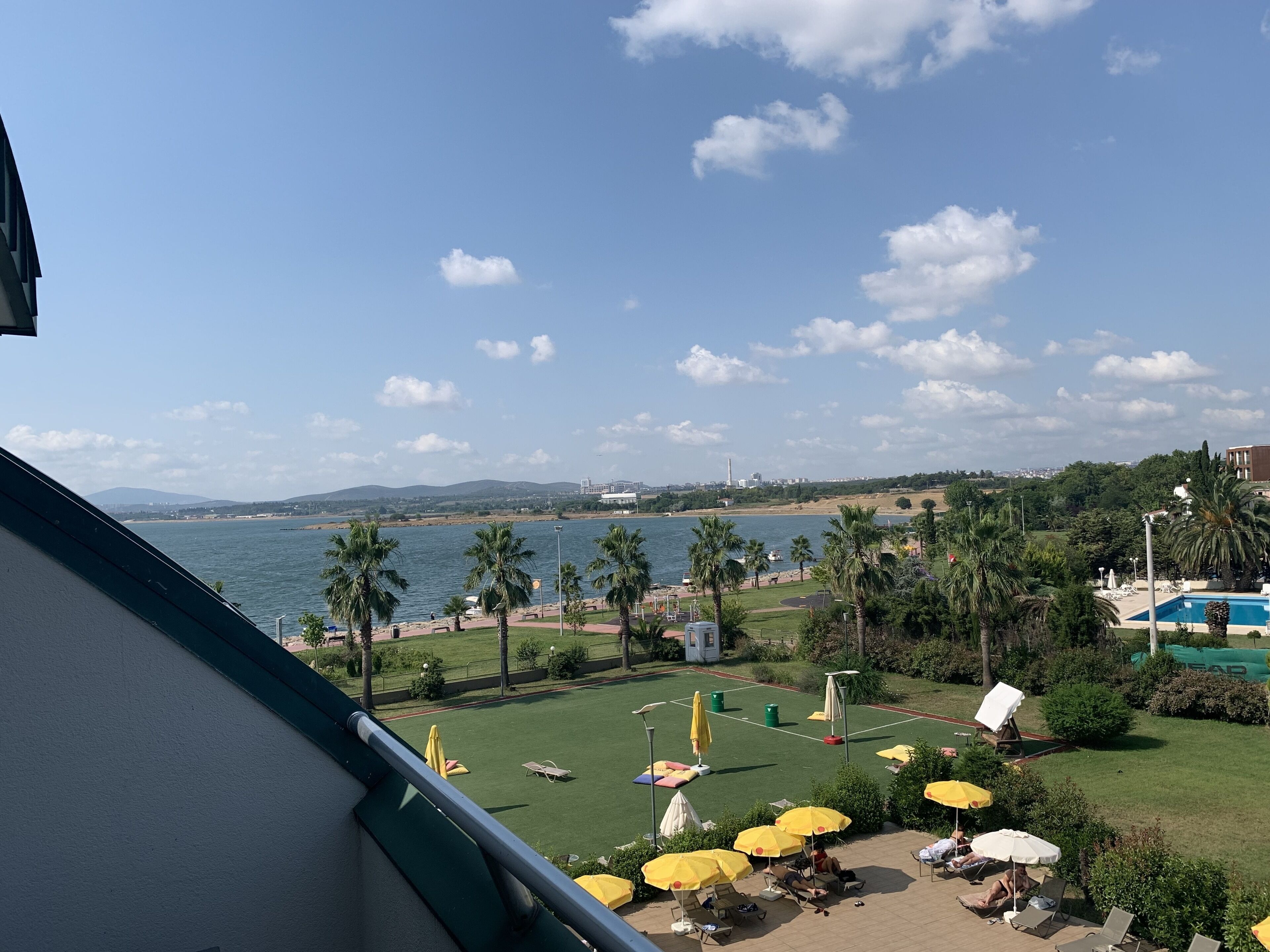 A balcony with a view of a beach, palm trees, and a pool area with umbrellas.
