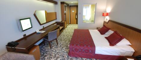 A hotel room with a bed, desk, chair, and a large mirror.