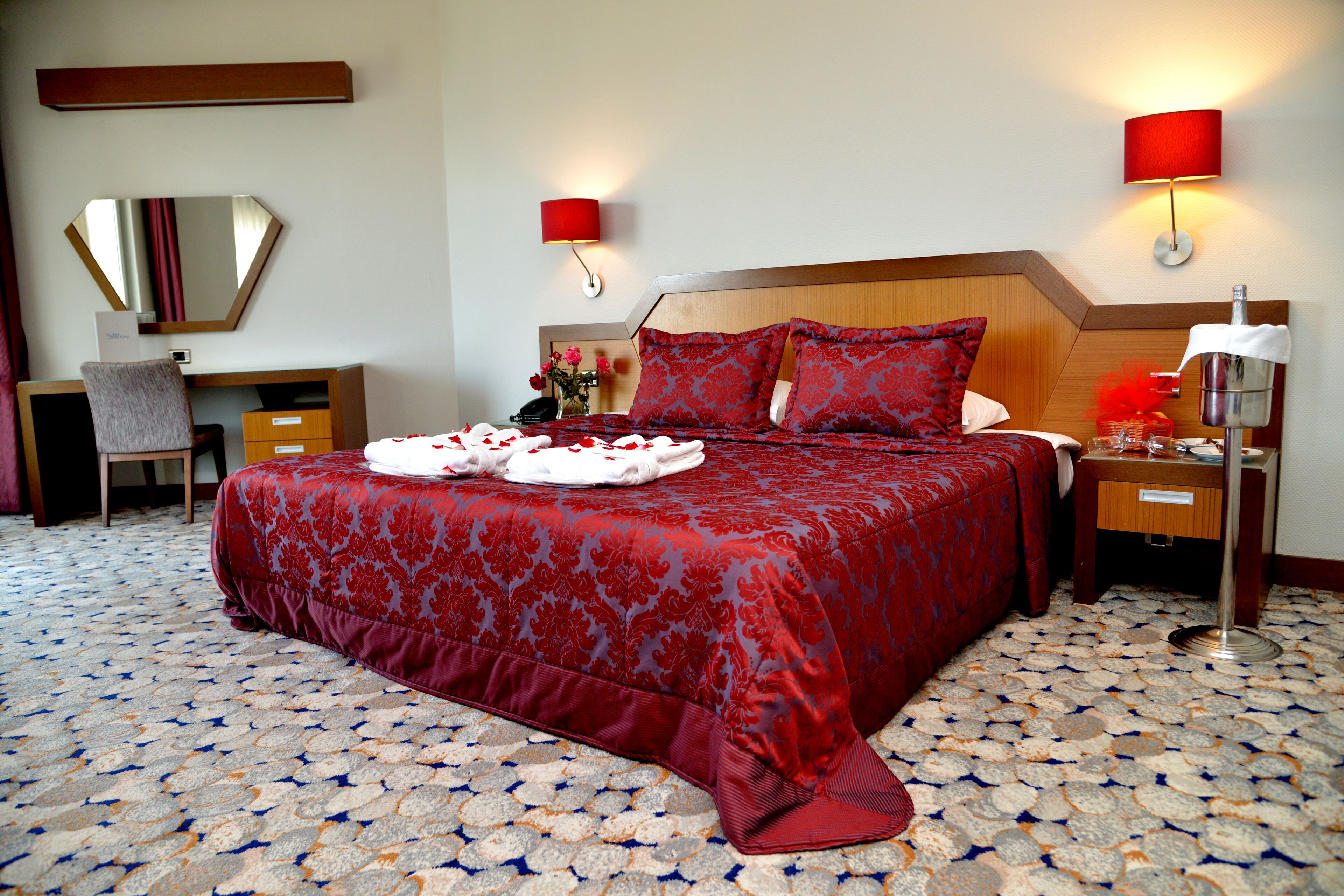 Habitación de hotel con una cama grande, un escritorio, una silla, un espejo y dos lámparas de noche.