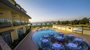 Un espace aménagé au bord de la piscine avec des tables et des chaises, une piscine protégée par des parois en verre et une vue sur la mer.