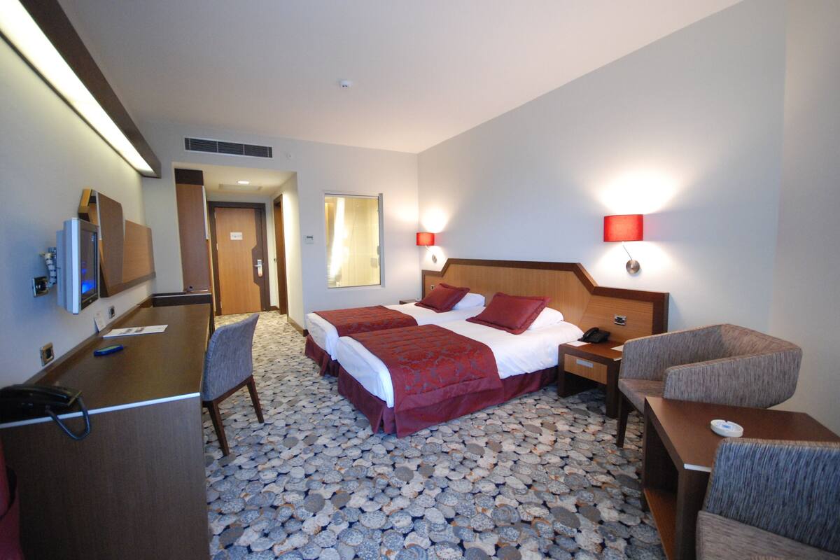 Una habitación de hotel con una cama grande, dos mesitas de noche, un escritorio, una silla y un televisor.