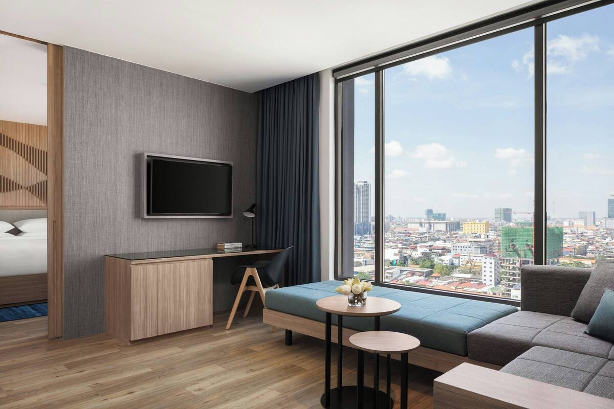 Una habitación de hotel moderna con un ventanal grande, una cama, un escritorio y un sofá.