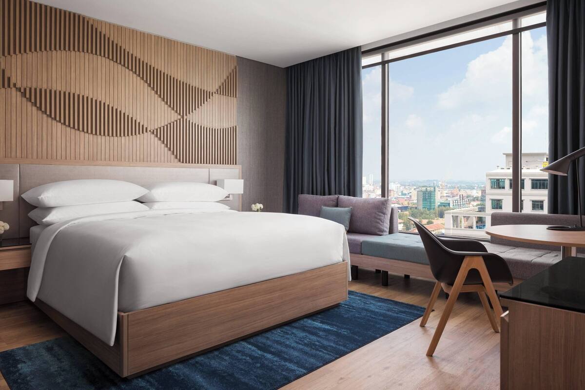 Habitación de hotel moderna con una cama grande, un escritorio y vistas a la ciudad.