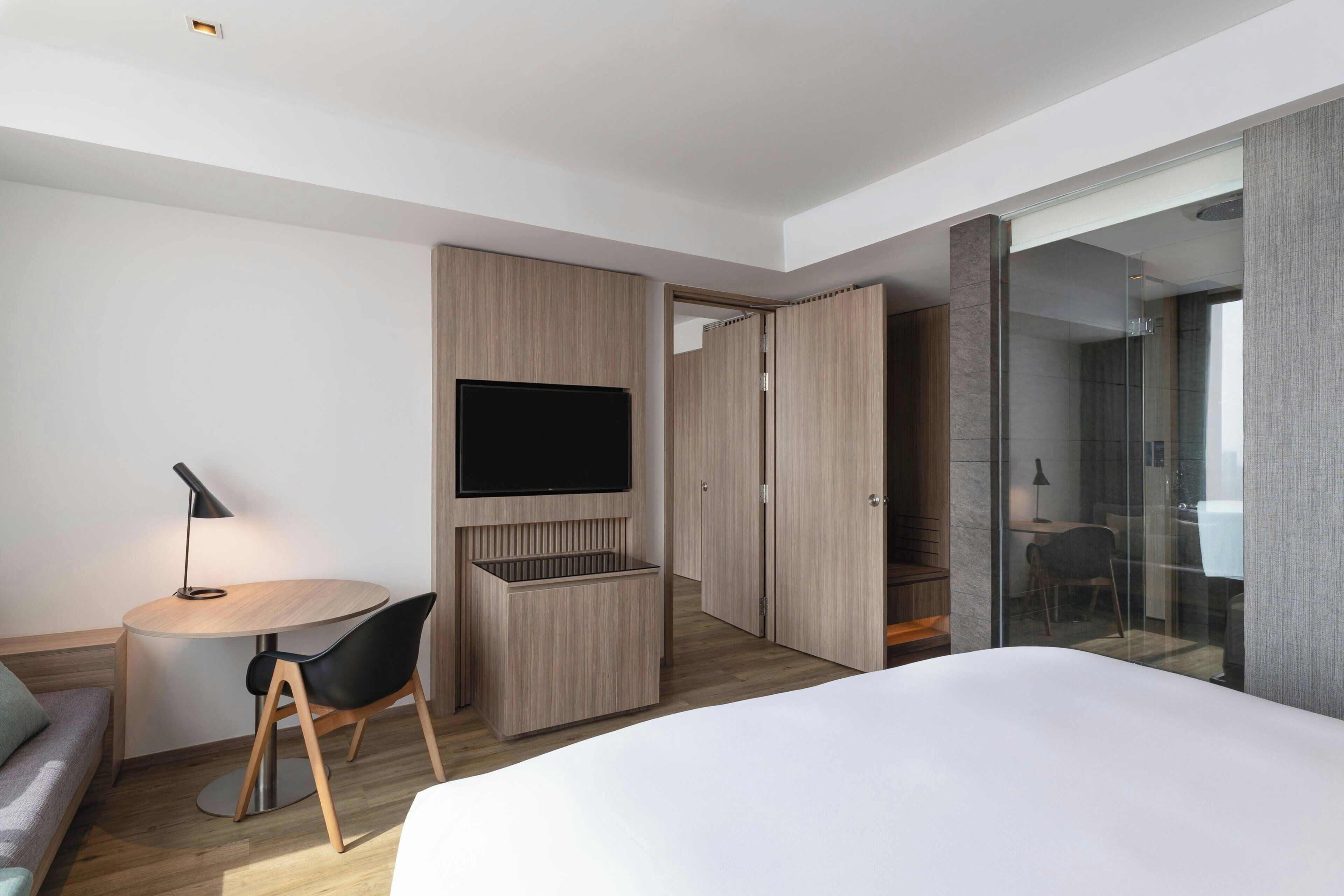 A modern hotel room with a bed, a desk, a chair, a TV, and a wardrobe.
