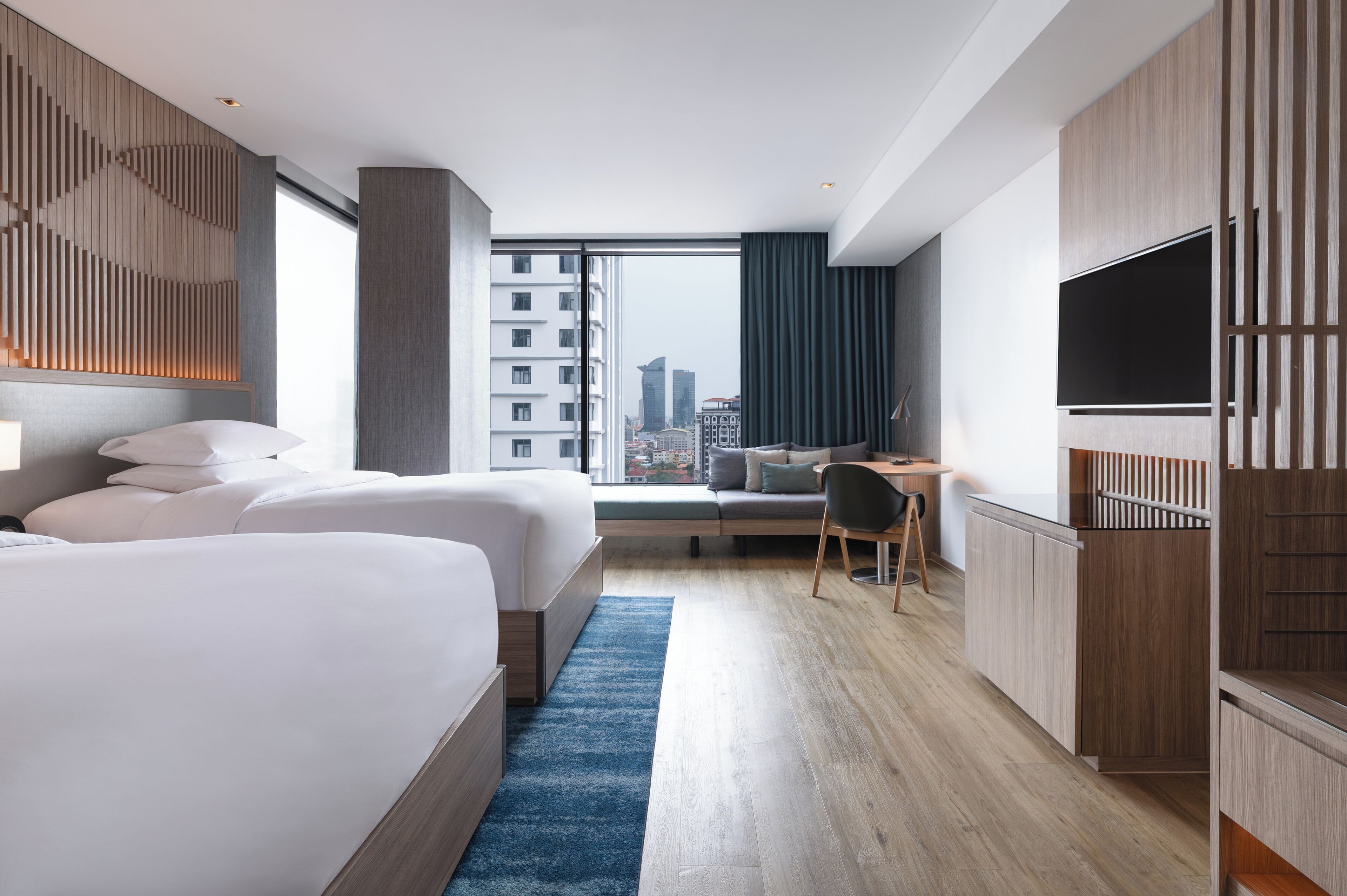 A modern hotel room with a large bed, a desk, a chair, a TV, and a view of the city.