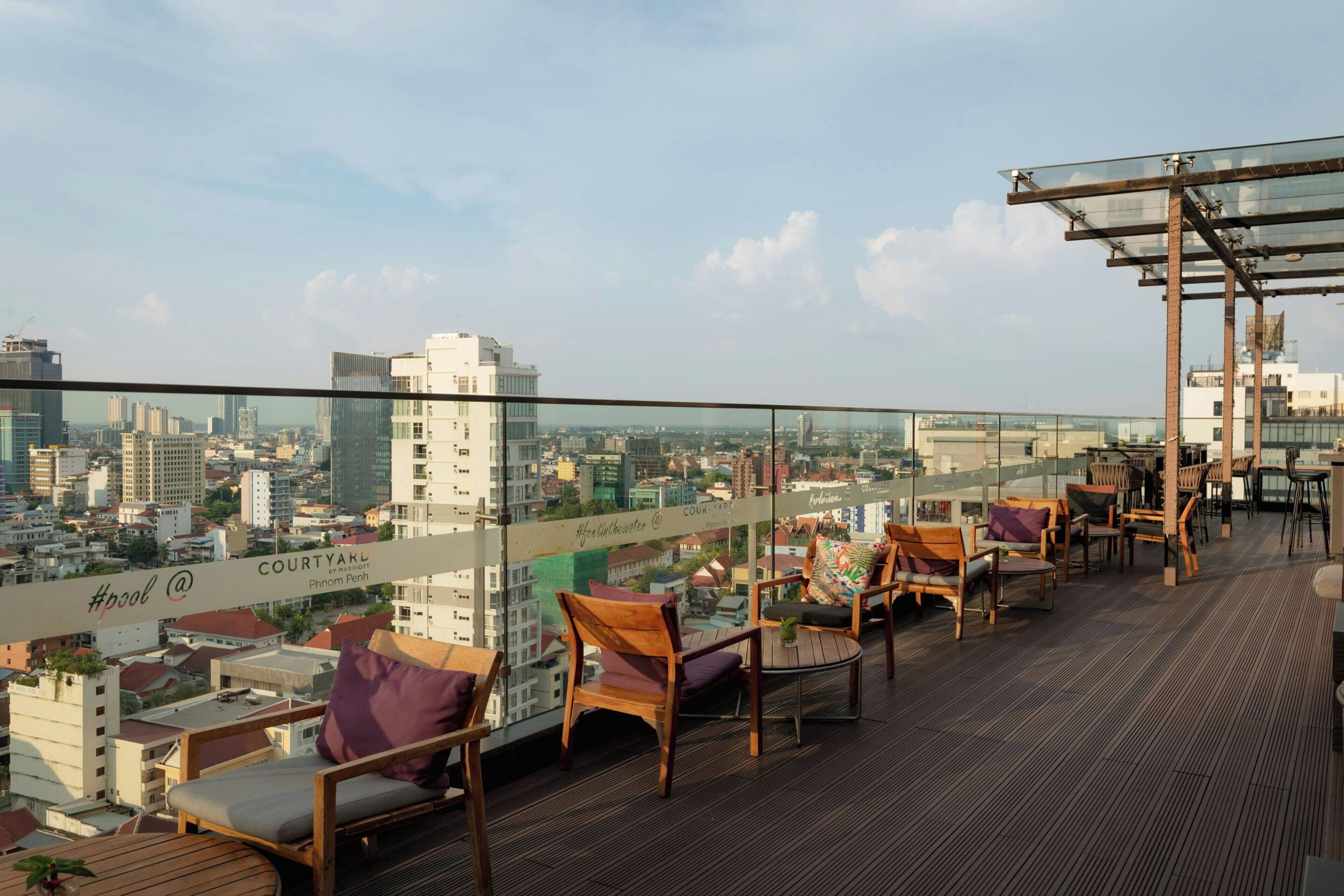 Terraza en la azotea con mobiliario exterior, barandilla de cristal y vistas a la ciudad.
