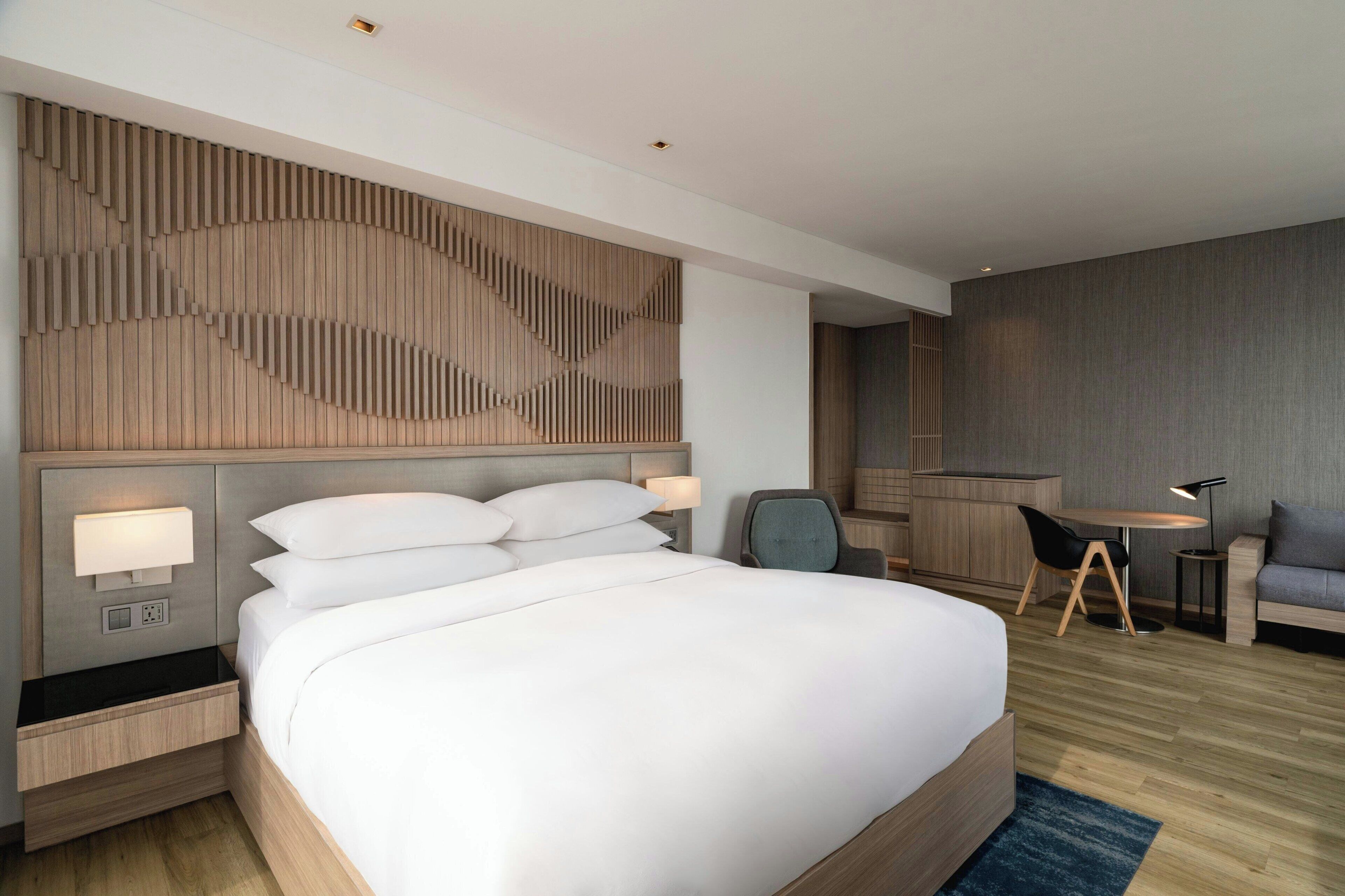 A modern hotel room with a large bed, bedside tables, a desk, and a chair.