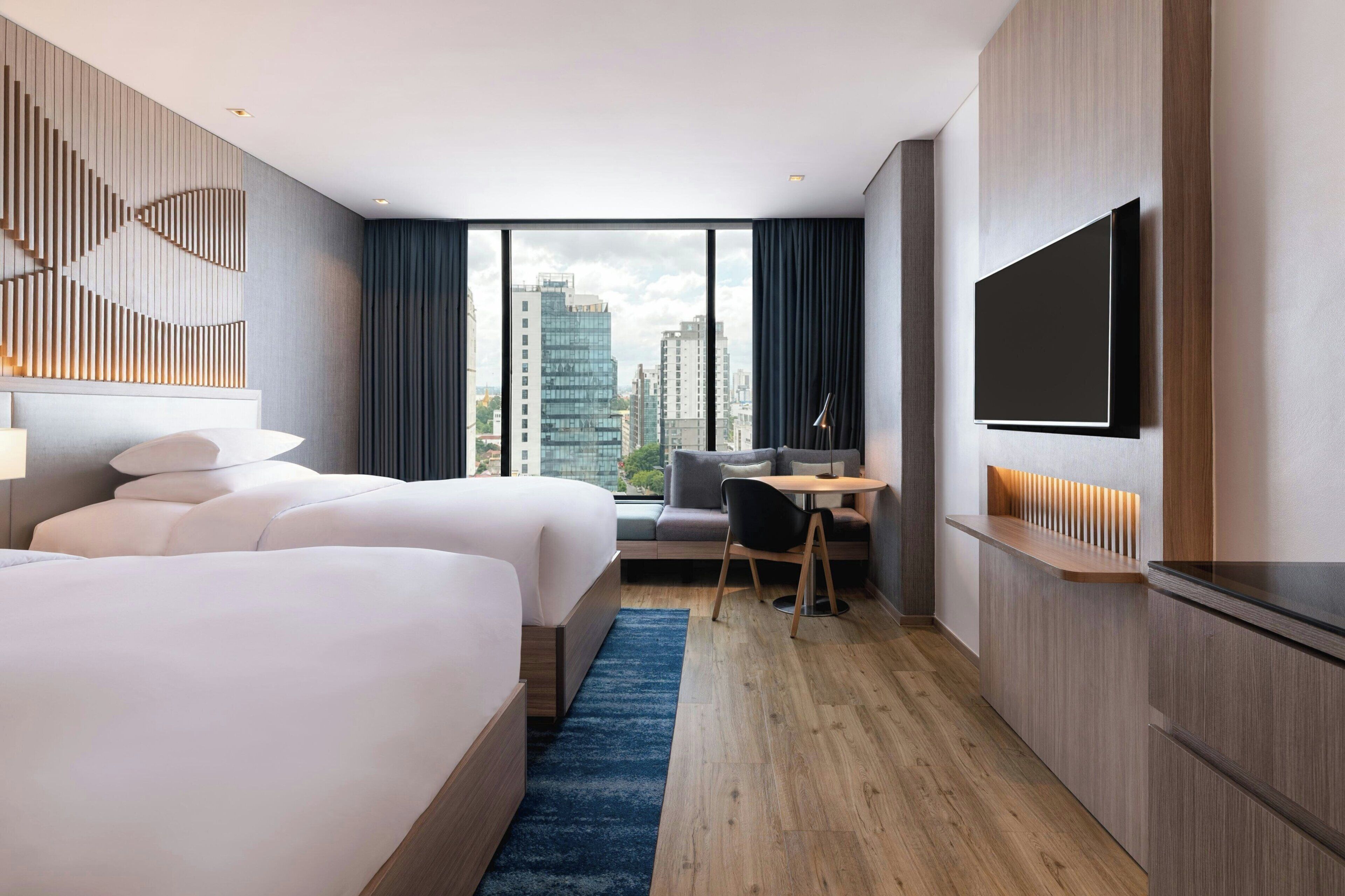 Habitación de hotel con cama, escritorio, silla, televisor y vistas a la ciudad.