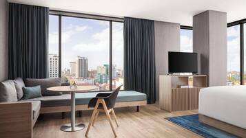 Une chambre d’hôtel moderne dotée d’une grande fenêtre, d’un canapé, d’une table à manger, d’un téléviseur et d’un lit.