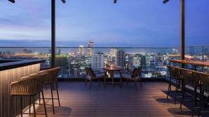 A rooftop bar with a city view, wooden furniture, and a glass railing. - Courtyard by Marriott Phnom Penh (Phnom Penh)