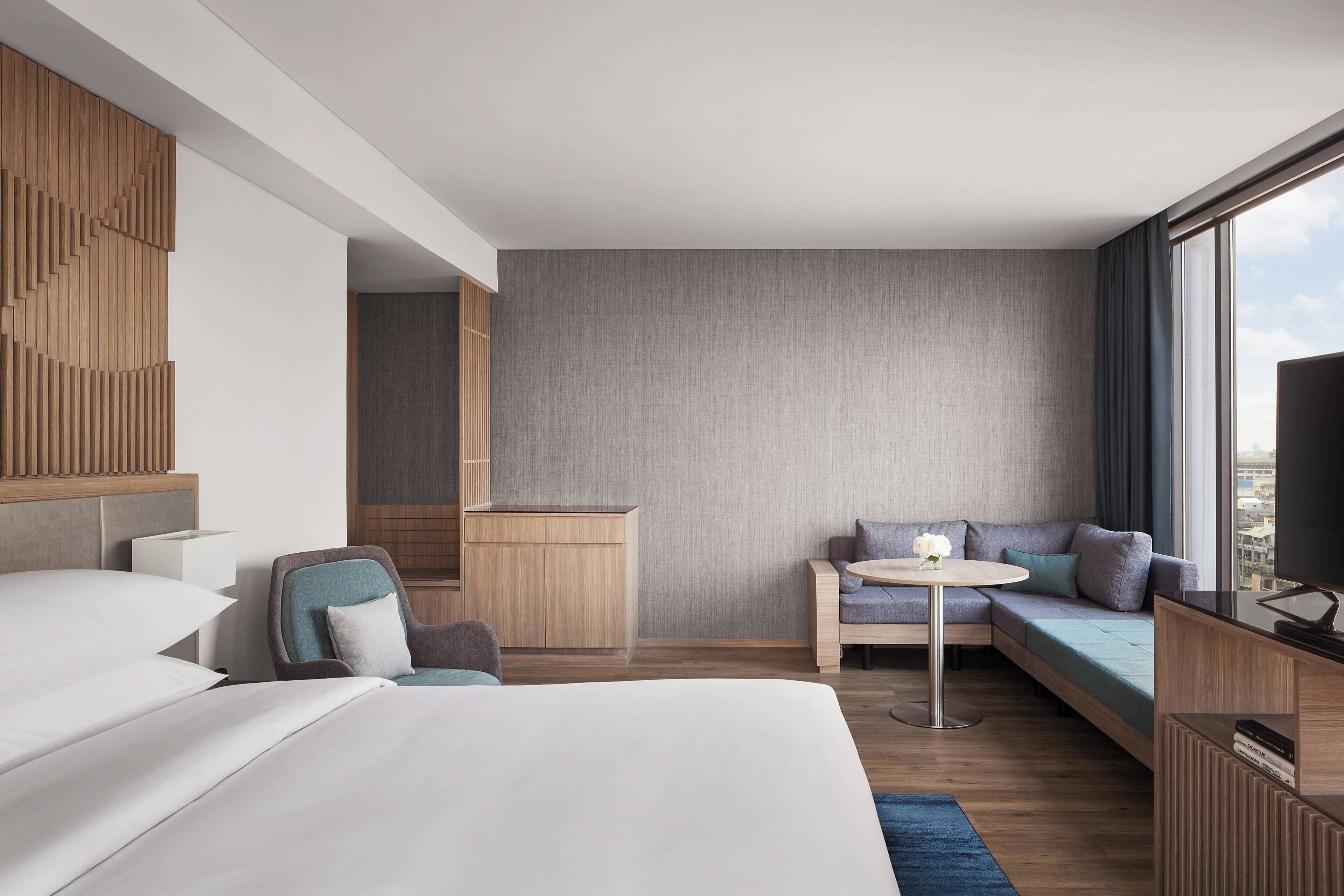 A modern hotel room with a large bed, a sofa, a small table, and a TV.