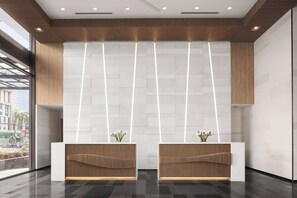 A reception area with two wooden reception desks, a modern ceiling design, and a view of the street through large windows.
