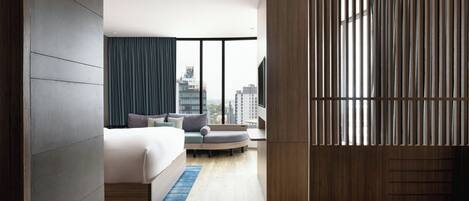 A modern hotel room with a bed, seating area, and a view of the city.