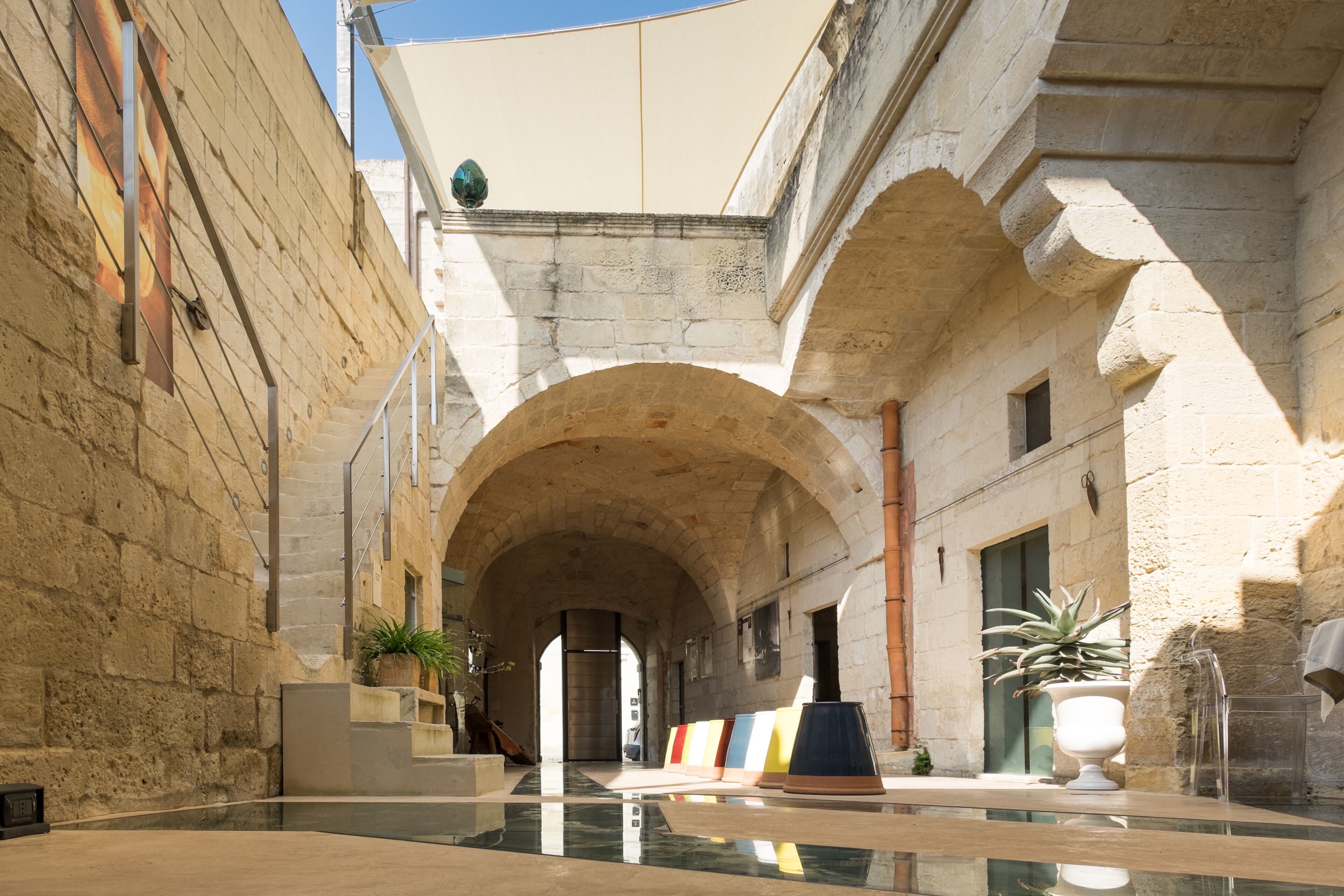 Un patio con arcos de piedra, un estanque reflectante y plantas en macetas.