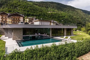 A modern house with a swimming pool, glass walls, and a view of a forested mountain. - Gaia Wellness Residence Hotel (Mezzana)