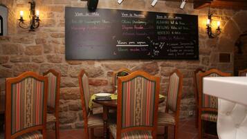 A restaurant with a stone wall, wooden chairs, and a chalkboard menu listing various wines and dishes.