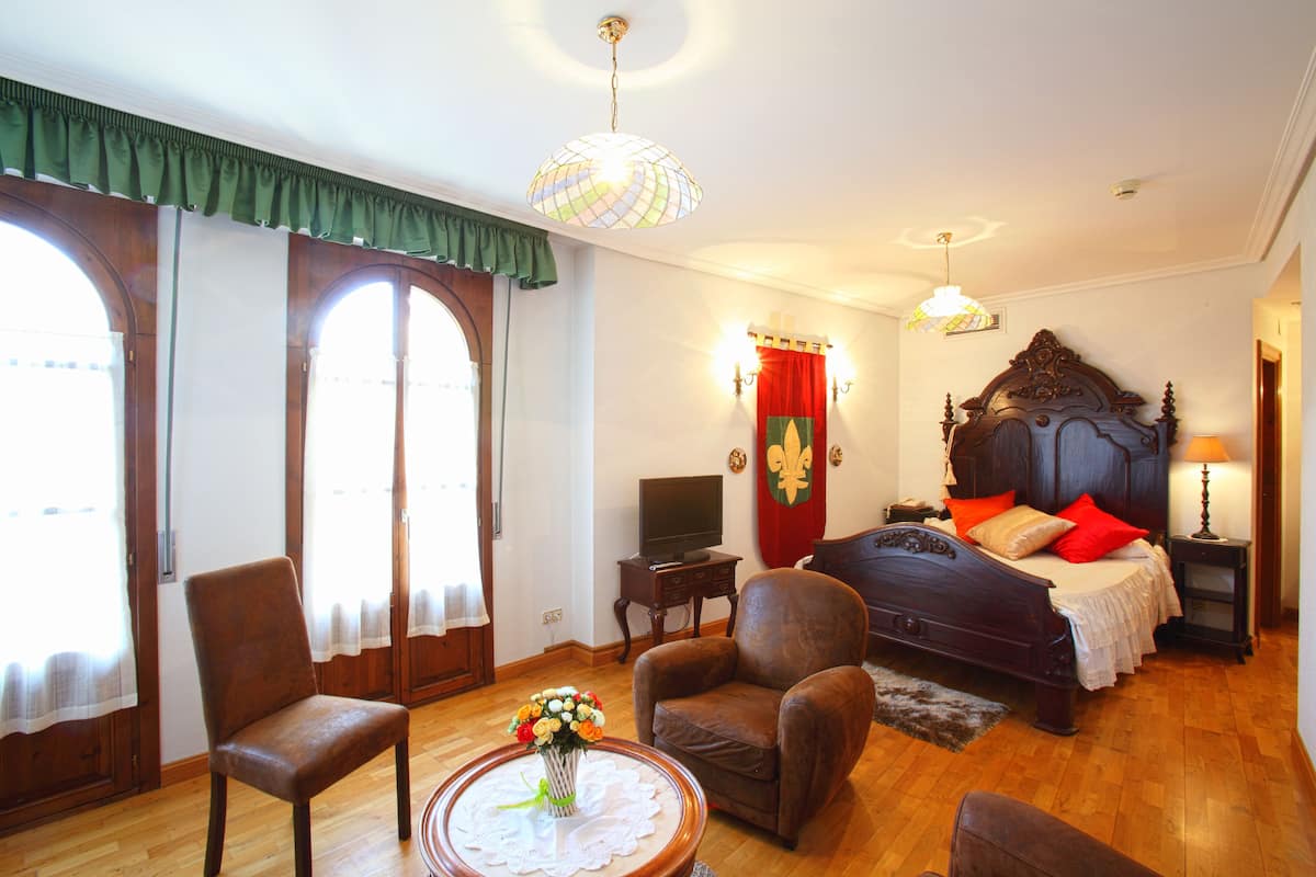 Un dormitorio con una cama grande, una silla, un televisor y una mesa con un jarrón de flores.