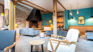A spacious lounge area with modern furniture, a stone wall, and a fireplace. - Hôtel Club MMV Les Bergers (Huez)