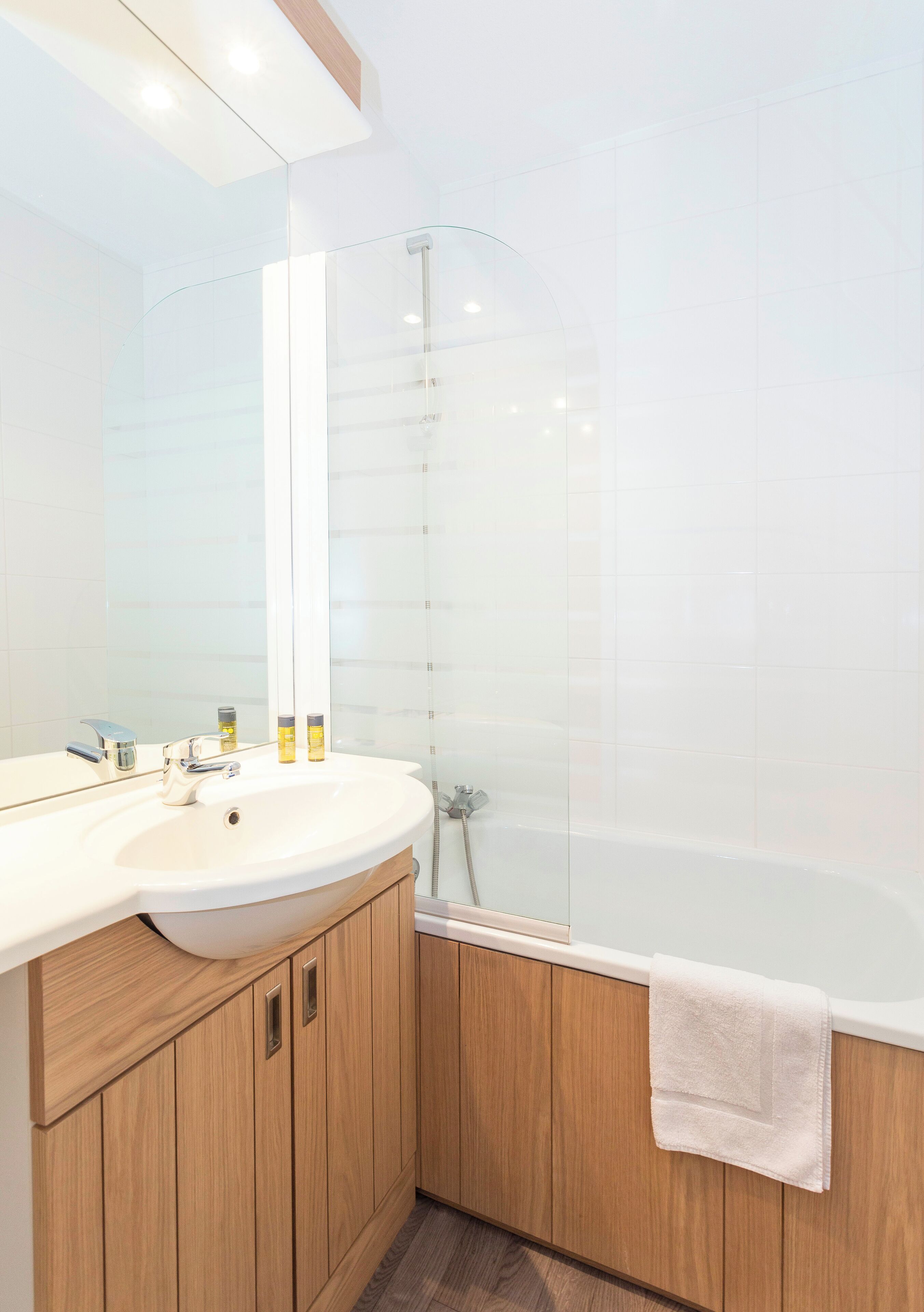 A modern bathroom with a wooden vanity, a large mirror, a glass shower enclosure, and a white bathtub.