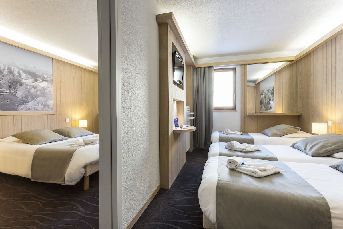 A hotel room with two beds, a small desk, a TV, and a window with curtains.