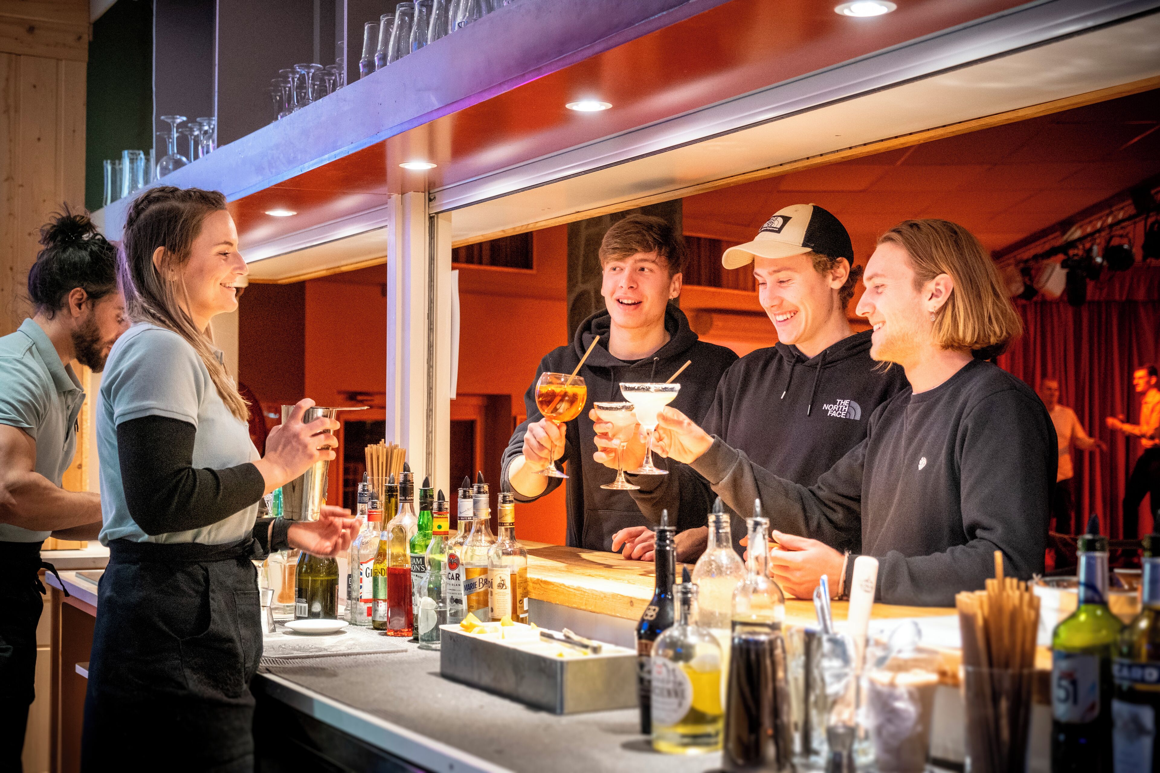 A bar area with a counter, various bottles, glasses, and a person serving drinks.
