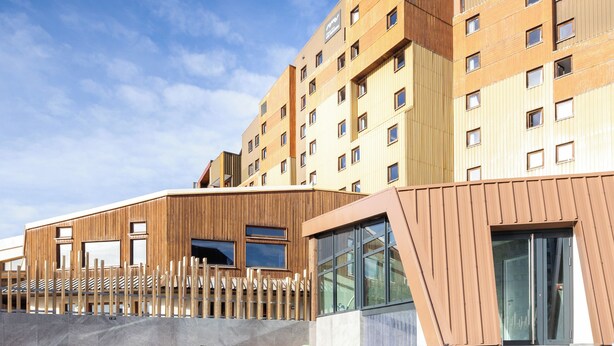 A modern hotel with a pool area, featuring a large building with multiple windows and a wooden facade. - Hôtel Club MMV Les Bergers (Huez)