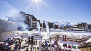 A snowy outdoor area with people gathered around tables and chairs, overlooking a mountainous landscape. - Hôtel Club MMV Les Bergers (Huez)