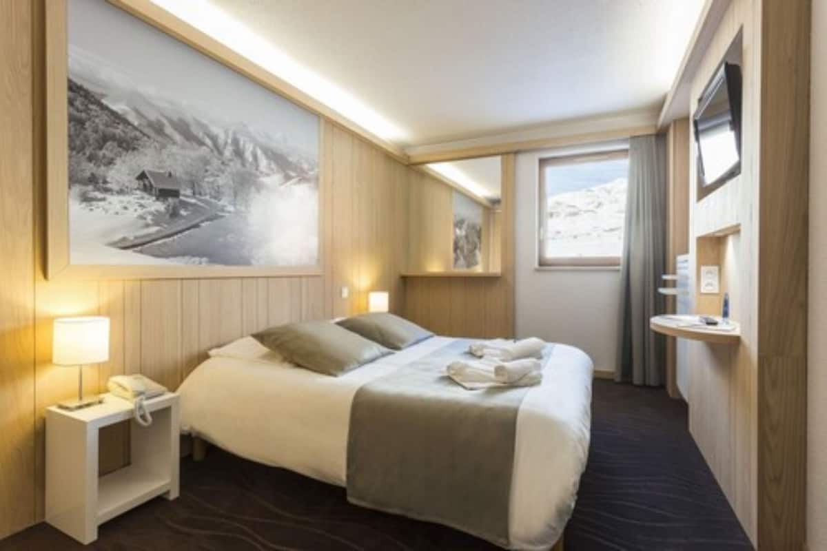 A hotel room with a bed, bedside table, lamp, and a large framed picture on the wall.