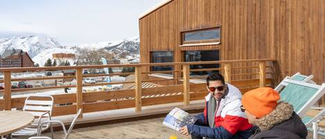 A wooden deck with metal chairs and a table, overlooking a snowy mountain landscape.